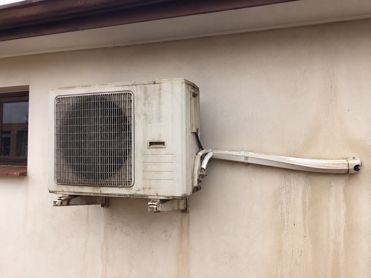 Old non-inverter outdoor unit, rusted and streaking a stained wall